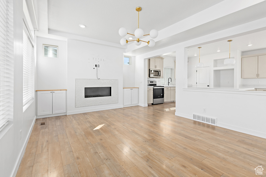 Unfurnished living room with a chandelier, a glass covered fireplace, light wood-style flooring, and recessed lighting
