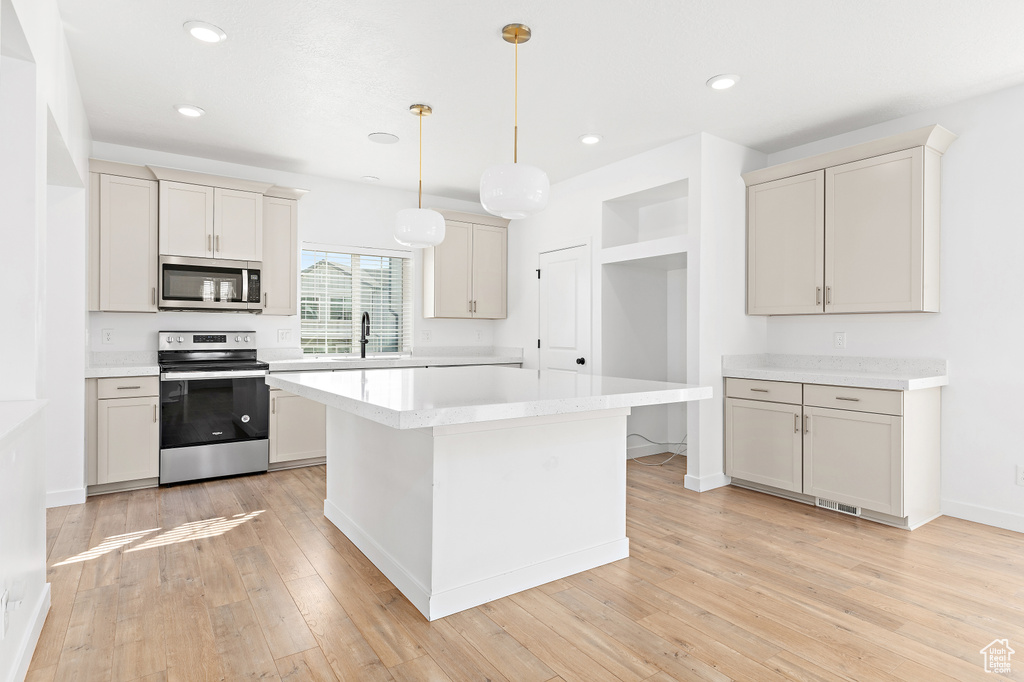 Kitchen with stainless steel appliances, light countertops, light wood-type flooring, a kitchen island, and hanging light fixtures