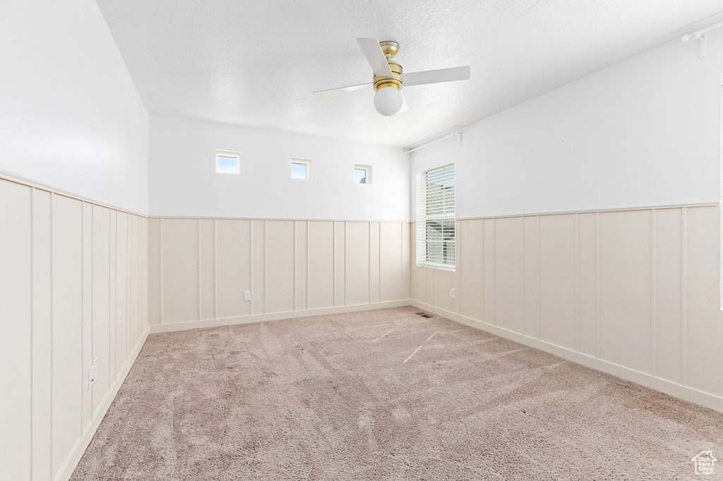 Empty room with a ceiling fan, carpet flooring, wainscoting, plenty of natural light, and a decorative wall