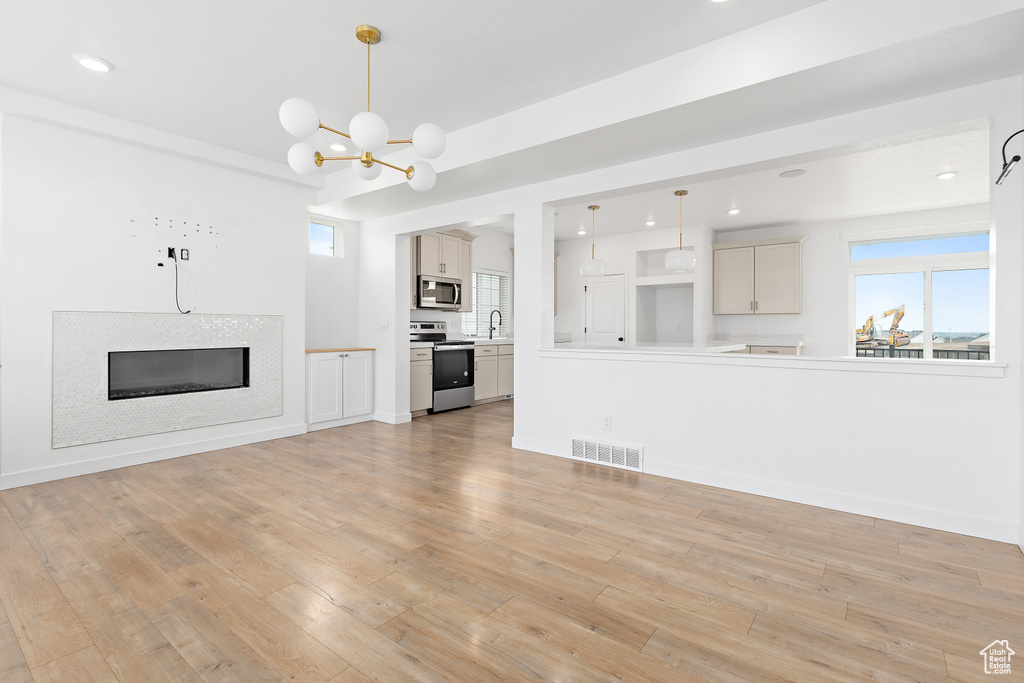 Unfurnished living room with light wood-style flooring, a chandelier, healthy amount of natural light, and recessed lighting