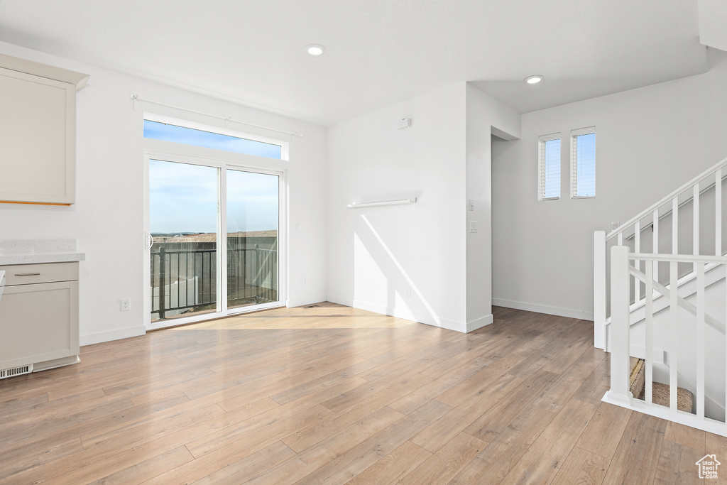 Unfurnished living room featuring light wood finished floors, recessed lighting, and stairway