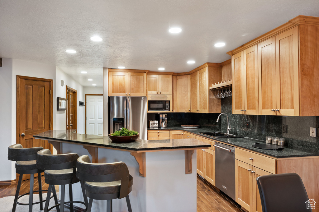 Kitchen featuring stainless steel appliances, wood finished floors, backsplash, a kitchen breakfast bar, and recessed lighting