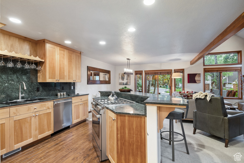 Kitchen featuring appliances with stainless steel finishes, a kitchen bar, recessed lighting, decorative backsplash, and wood finished floors