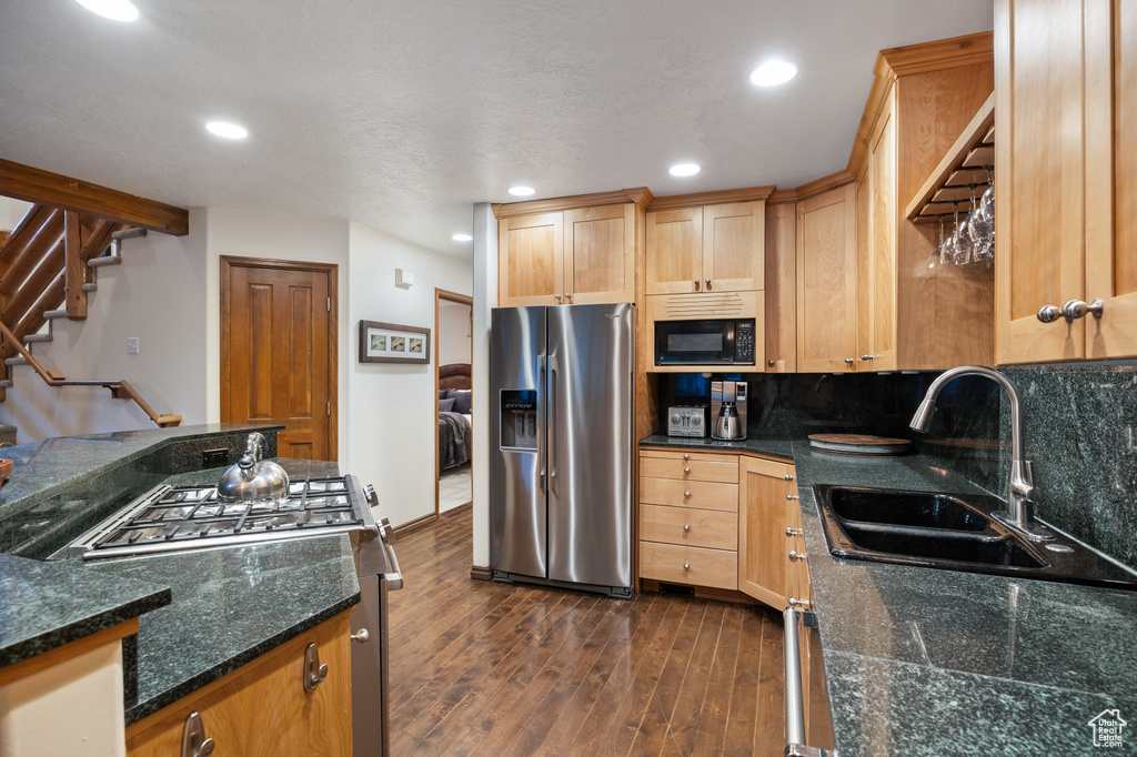 Kitchen featuring stainless steel refrigerator with ice dispenser, range, black microwave, dark wood-type flooring, and light brown cabinetry