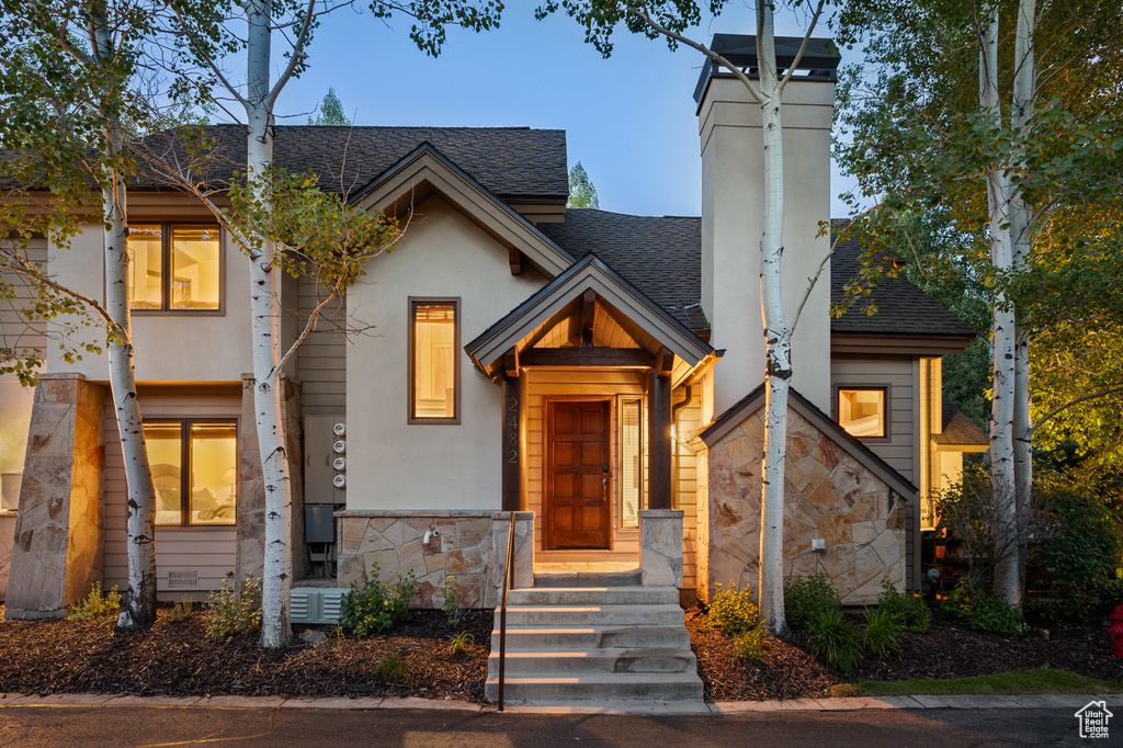 View of front of home with stone siding, a shingled roof, and a chimney