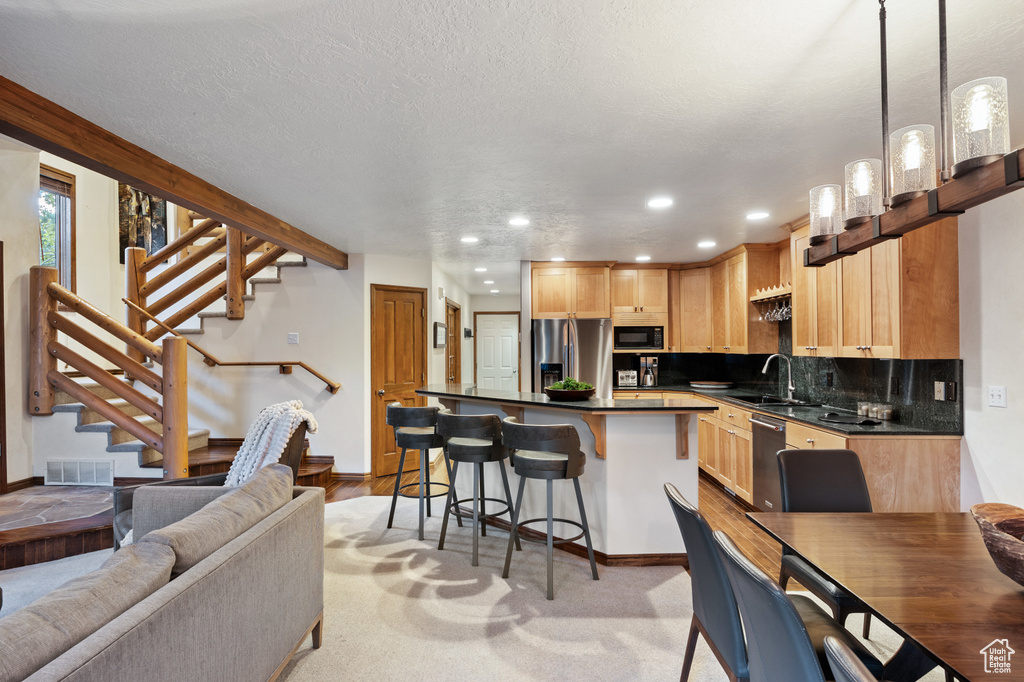 Kitchen featuring appliances with stainless steel finishes, dark countertops, a breakfast bar area, light brown cabinetry, and tasteful backsplash