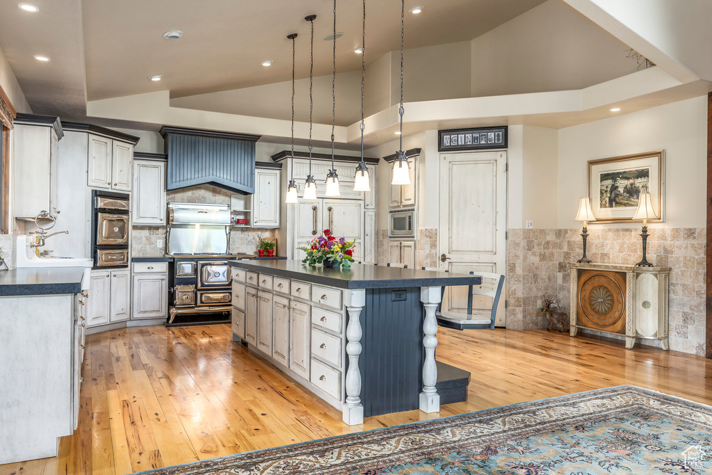 Kitchen featuring dark countertops, light wood-style flooring, appliances with stainless steel finishes, a breakfast bar area, and a kitchen island
