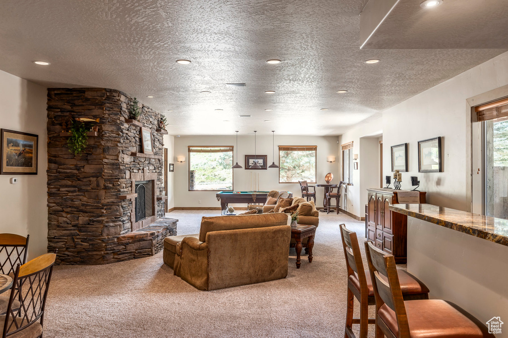 Living room with light carpet, billiards, a textured ceiling, a stone fireplace, and recessed lighting