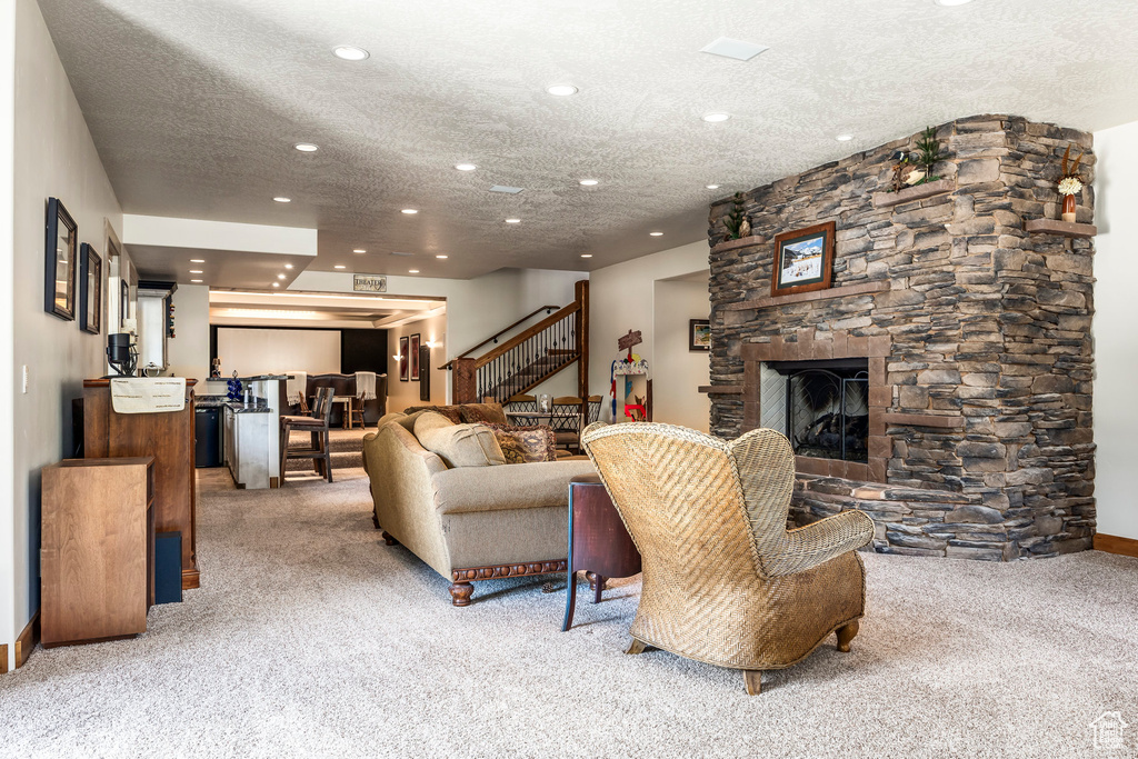 Carpeted living area with recessed lighting, stairway, a textured ceiling, and a stone fireplace