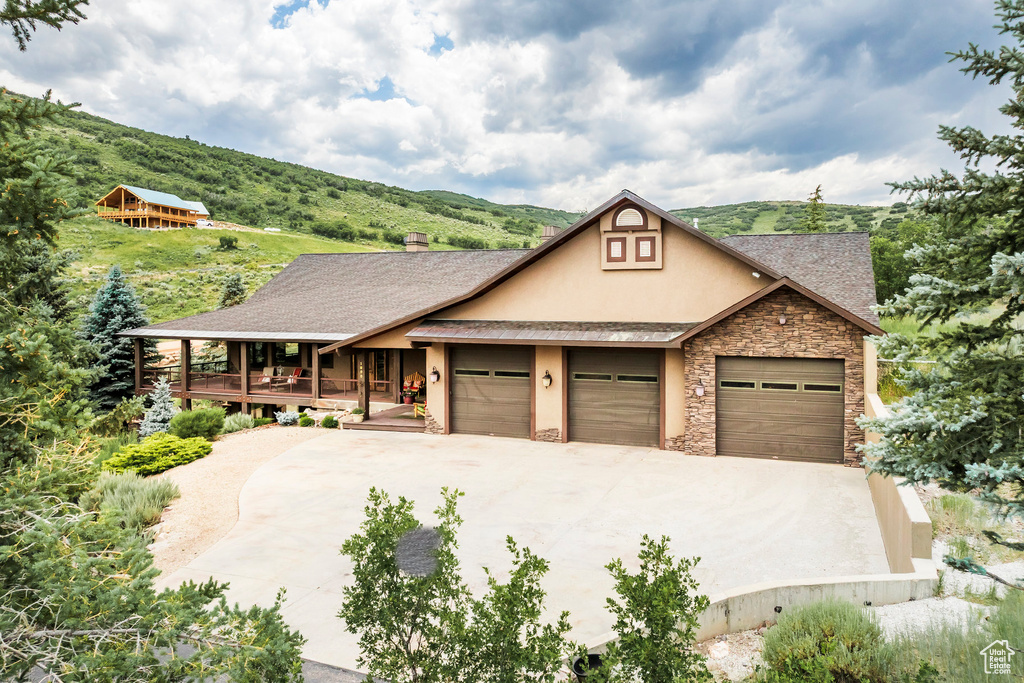 View of front facade with stucco siding, stone siding, concrete driveway, covered porch, and an attached garage