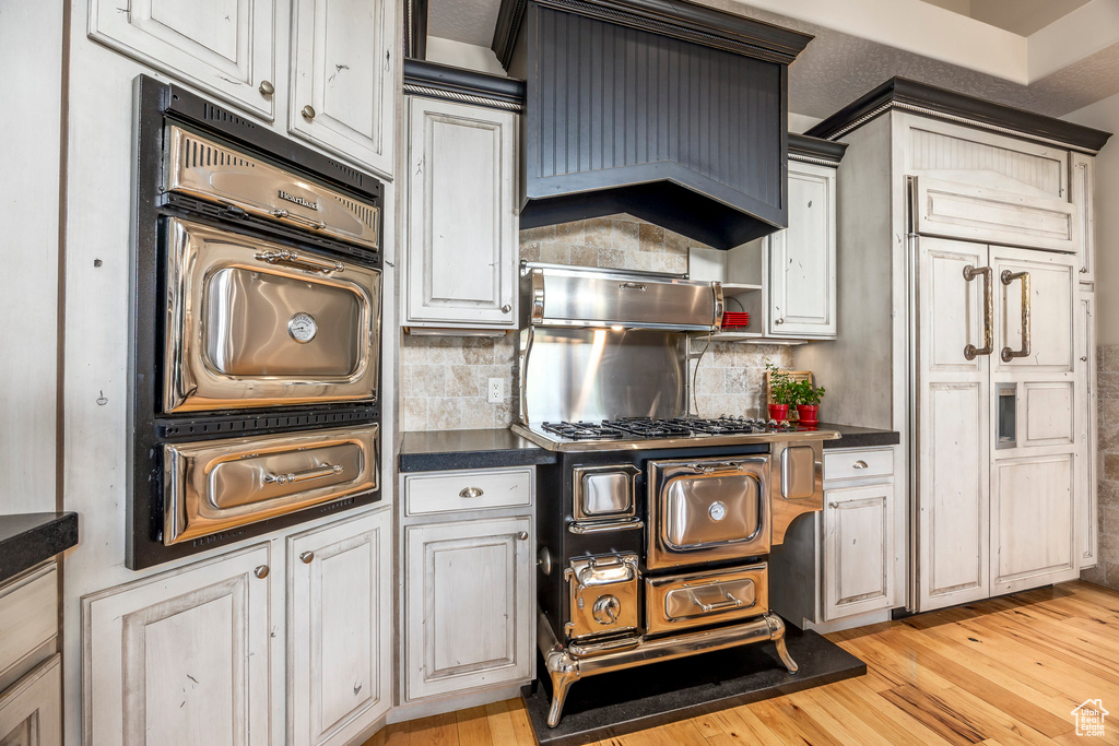 Kitchen with dark countertops, light wood finished floors, a warming drawer, and decorative backsplash