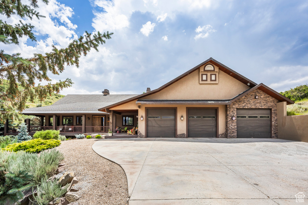 View of front of home featuring stucco siding, stone siding, driveway, a garage, and covered porch