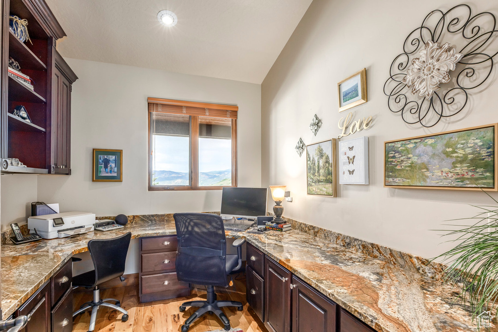 Home office featuring built in desk, vaulted ceiling, and light wood-style floors