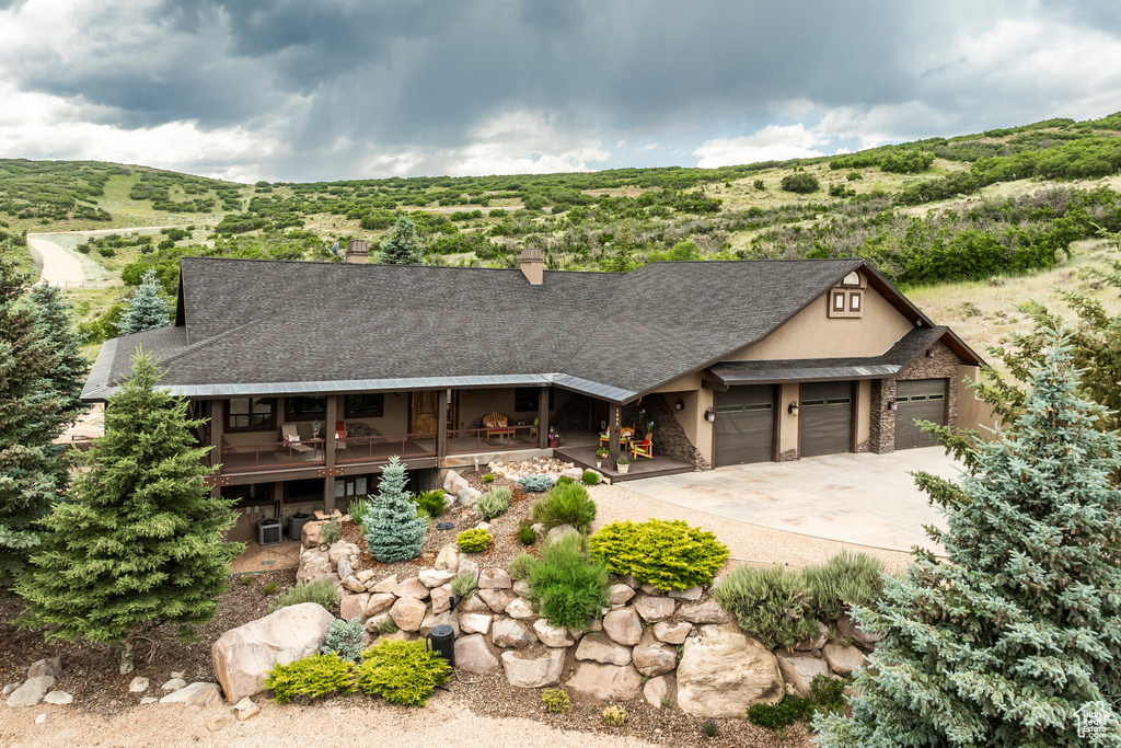 View of front of property featuring a garage, stucco siding, a shingled roof, a chimney, and driveway