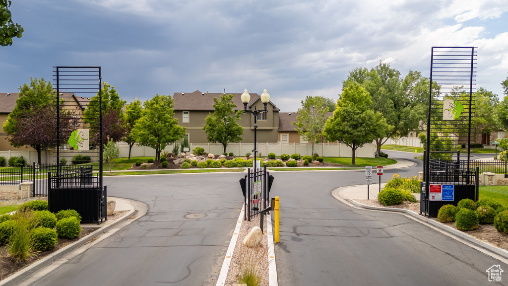 View of asphalt street featuring street lights, curbs, a residential view, a gate, and a gated entry