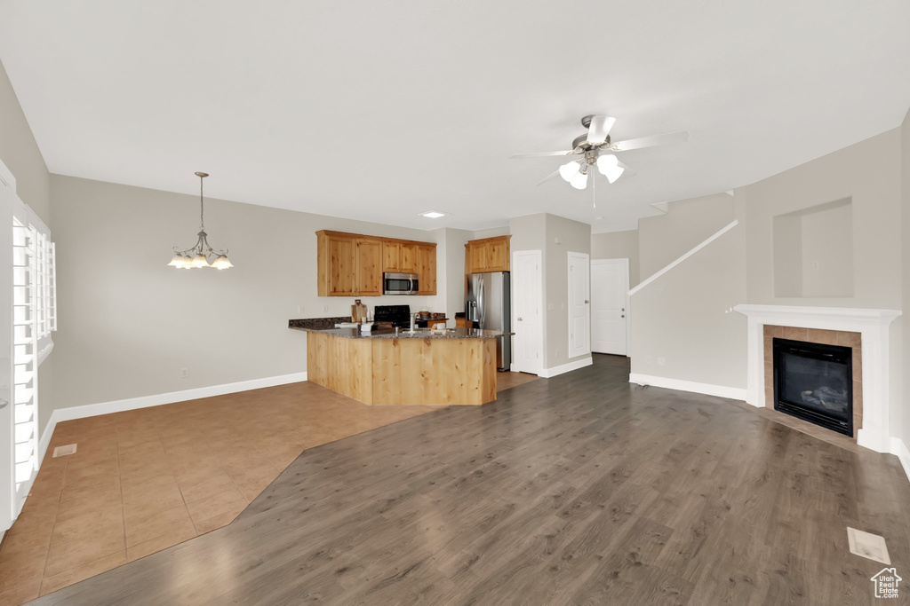 Unfurnished living room with a ceiling fan, a chandelier, a tile fireplace, and dark wood finished floors
