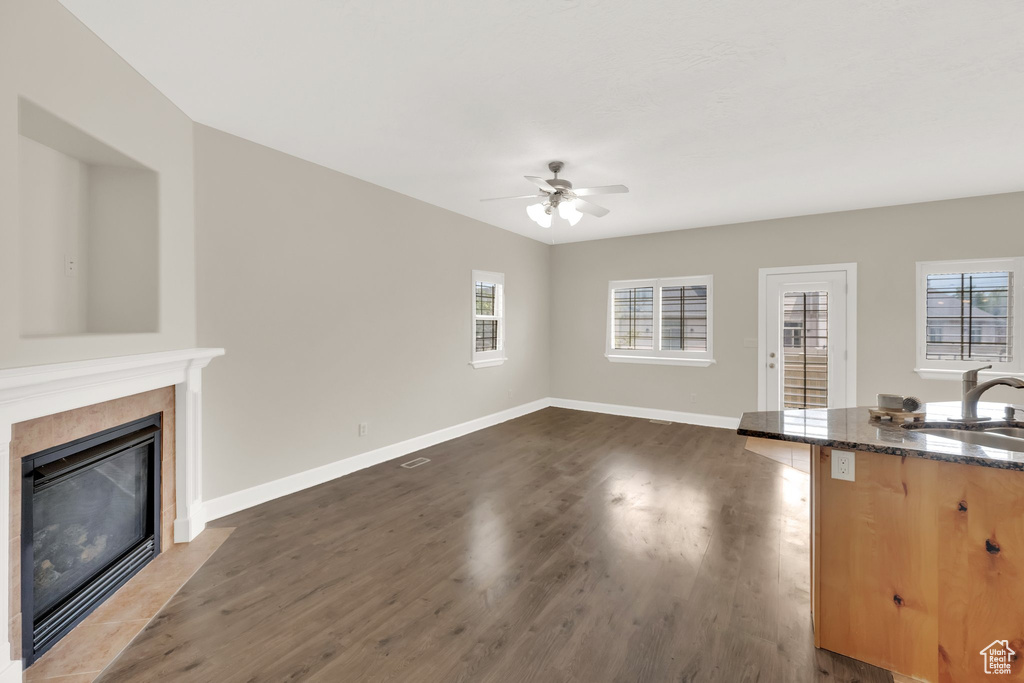 Unfurnished living room with a ceiling fan, a tiled fireplace, and dark wood-style floors