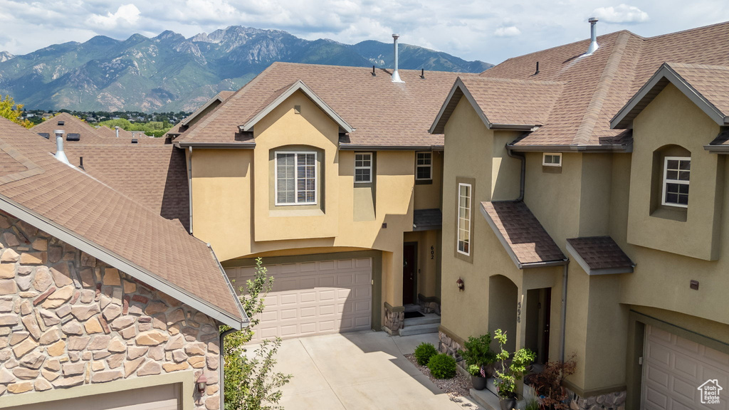 View of front of property with stucco siding, a mountain view, driveway, stone siding, and a garage