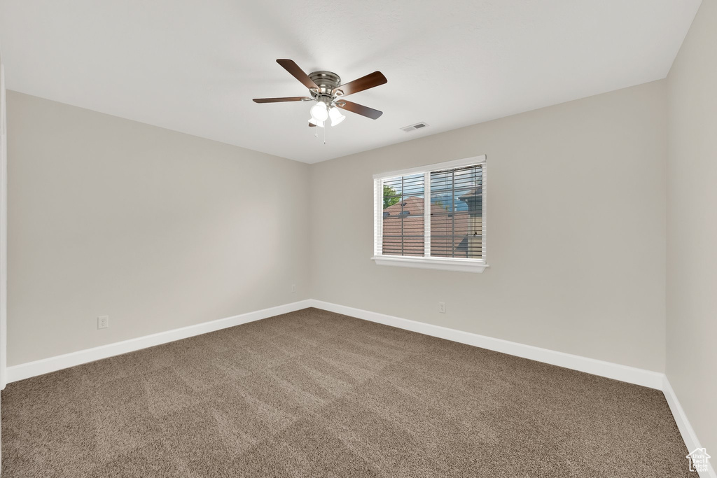 Empty room featuring dark colored carpet and ceiling fan