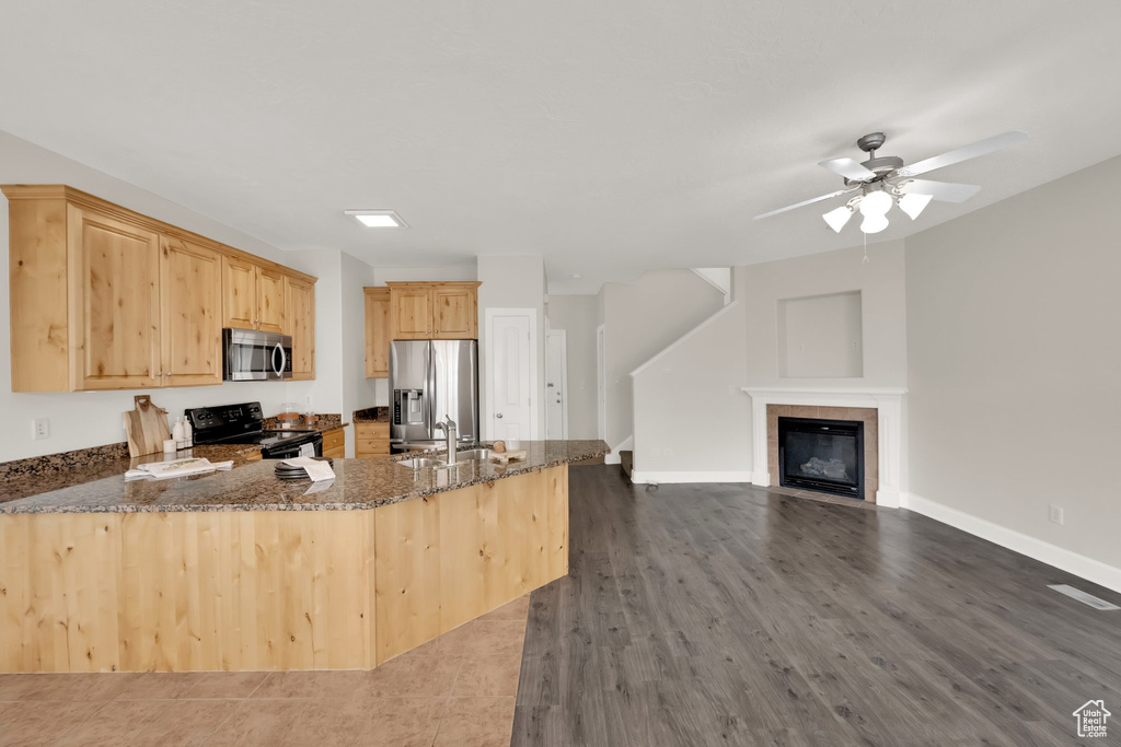 Kitchen featuring appliances with stainless steel finishes, dark stone counters, a peninsula, light brown cabinets, and ceiling fan