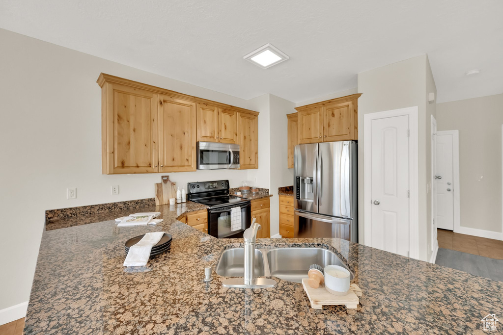 Kitchen with appliances with stainless steel finishes, dark stone counters, light brown cabinetry, and tile patterned floors