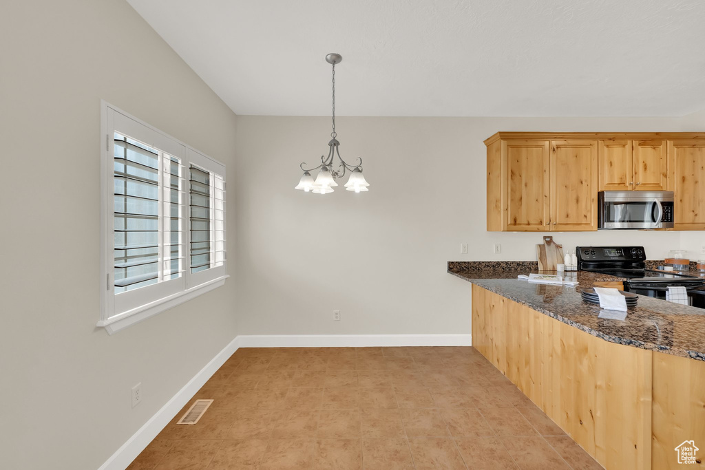 Kitchen featuring stainless steel microwave, black electric range, a chandelier, dark stone counters, and pendant lighting