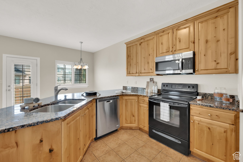 Kitchen with appliances with stainless steel finishes, light brown cabinetry, light tile patterned floors, a peninsula, and dark stone counters