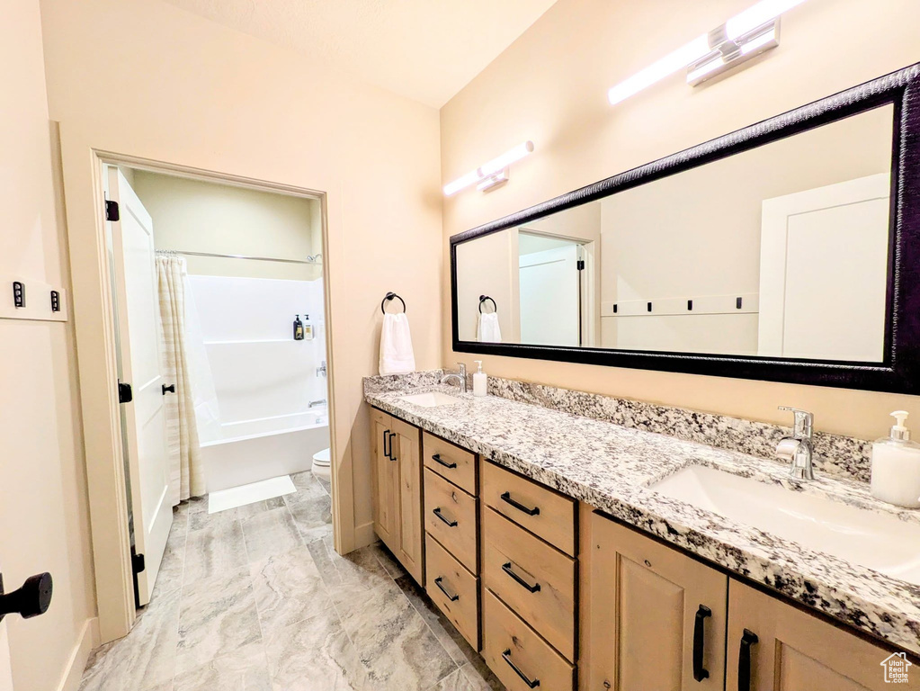 Bathroom with double vanity, shower / tub combo, and marble finish flooring