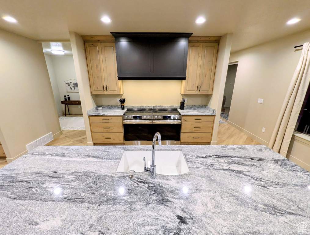 Kitchen with stainless steel electric stove, light brown cabinets, exhaust hood, light stone countertops, and recessed lighting