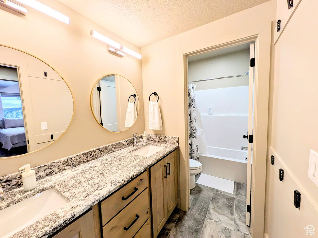 Ensuite bathroom featuring double vanity, shower / bathtub combination with curtain, and a textured ceiling
