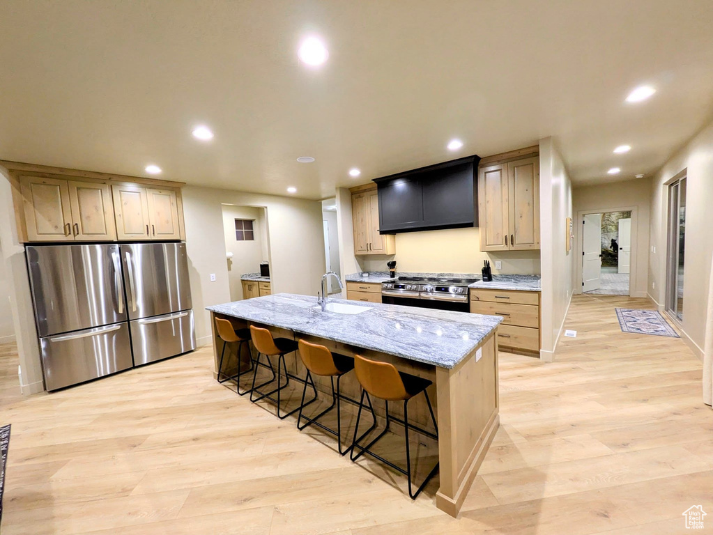 Kitchen with stainless steel appliances, exhaust hood, recessed lighting, light wood-type flooring, and a breakfast bar area