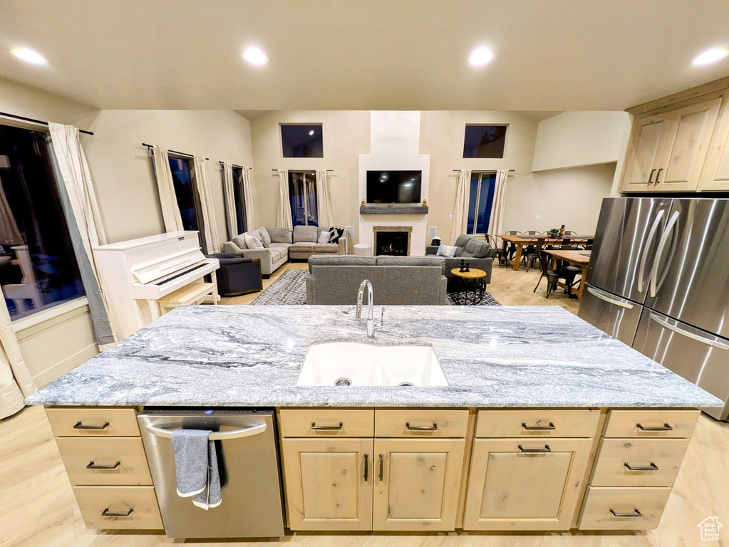 Kitchen with stainless steel appliances, light brown cabinetry, light stone counters, an island with sink, and recessed lighting