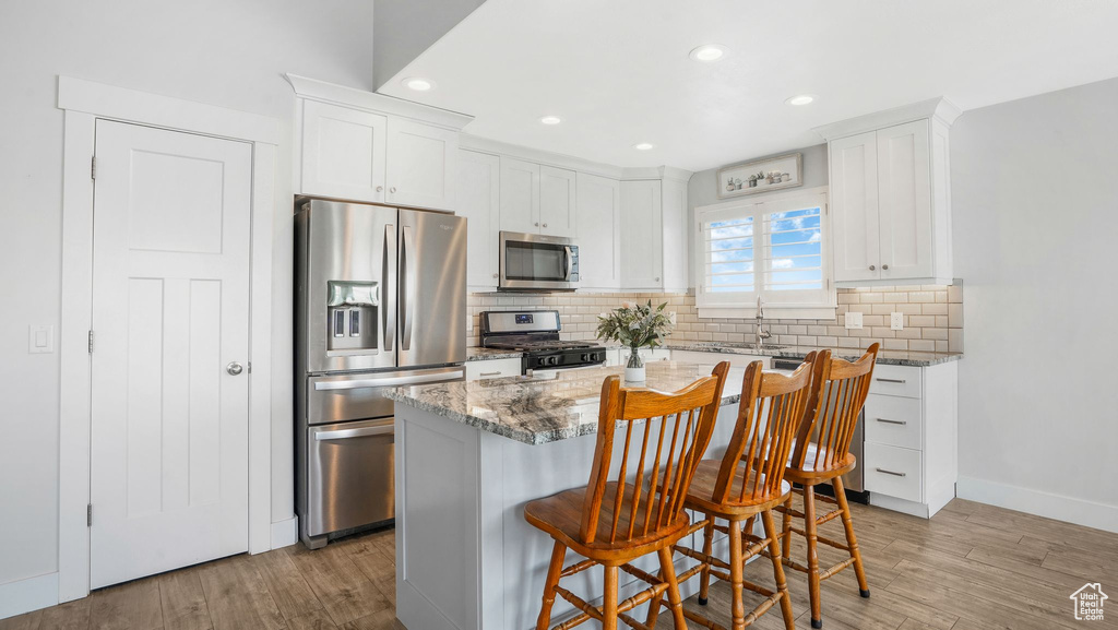 Kitchen with stainless steel appliances, light stone counters, white cabinetry, and recessed lighting