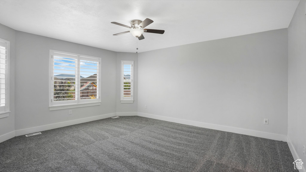 Carpeted empty room featuring ceiling fan and baseboards