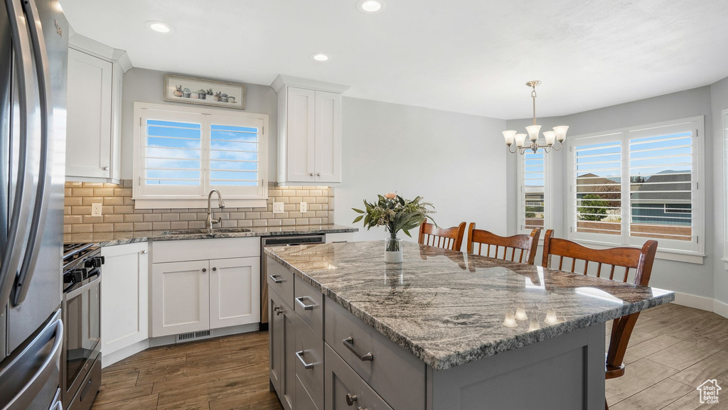 Kitchen featuring stainless steel appliances, a chandelier, a kitchen island, dark wood-type flooring, and backsplash