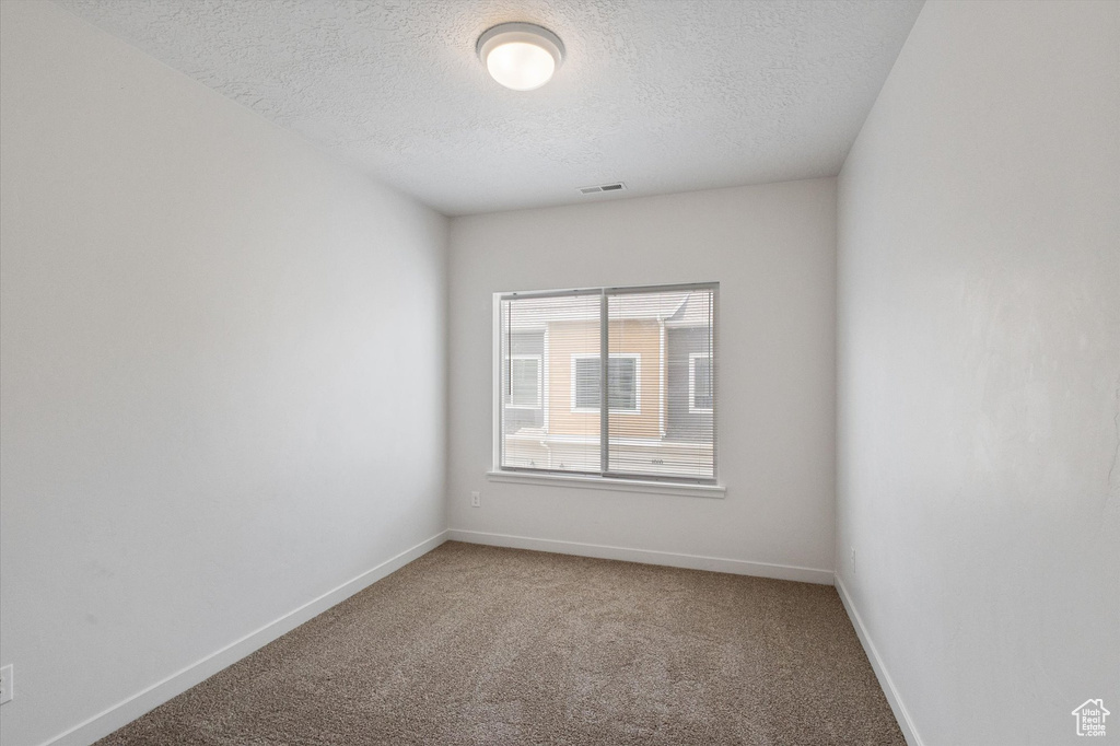 Empty room with a textured ceiling and light colored carpet