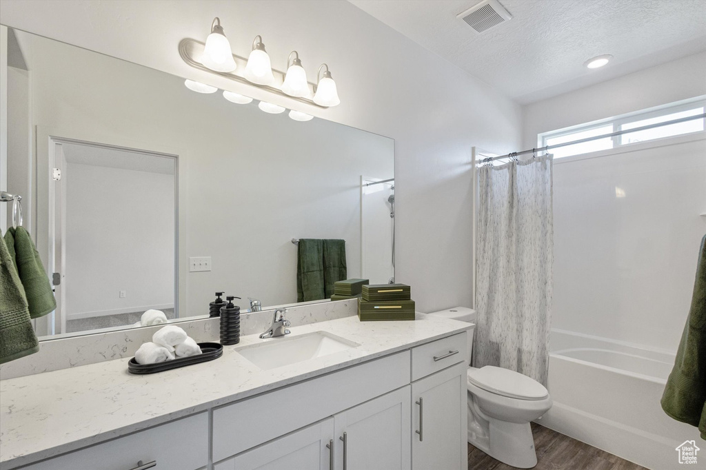 Full bath featuring wood finished floors, vanity, shower / bath combo with shower curtain, and a textured ceiling