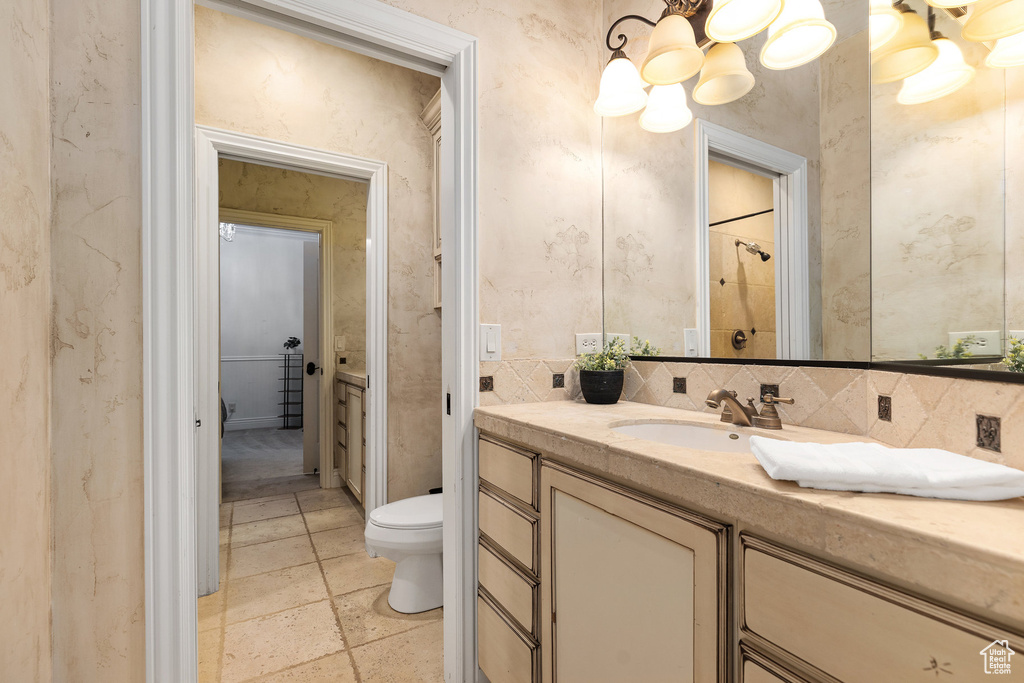 Full bath featuring a chandelier, vanity, tasteful backsplash, a shower, and stone tile floors