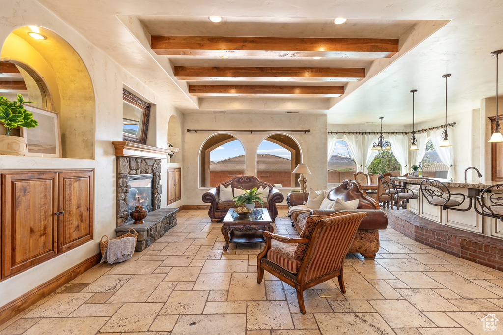 Living area featuring stone tile floors, beam ceiling, plenty of natural light, a stone fireplace, and recessed lighting
