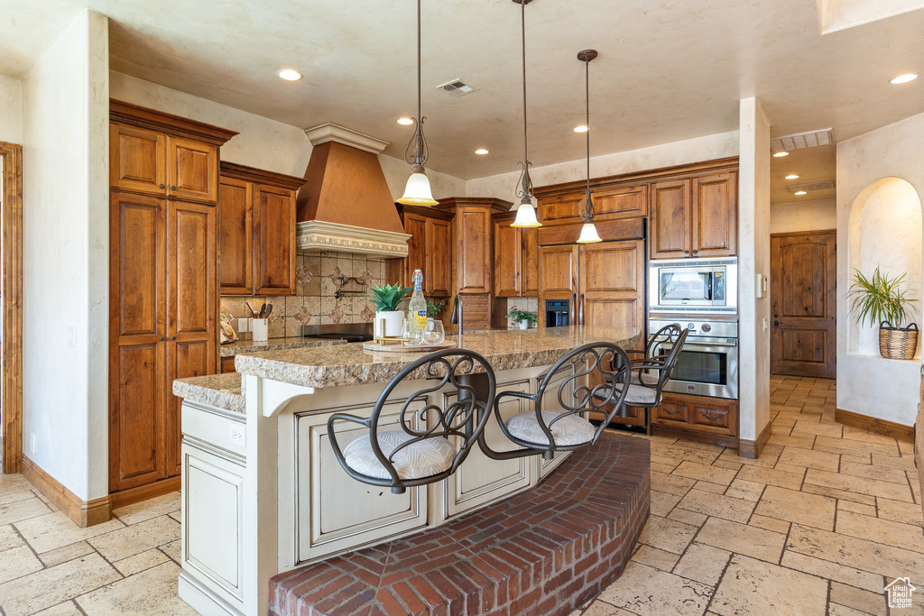 Kitchen with built in appliances, premium range hood, brown cabinetry, a kitchen bar, and recessed lighting
