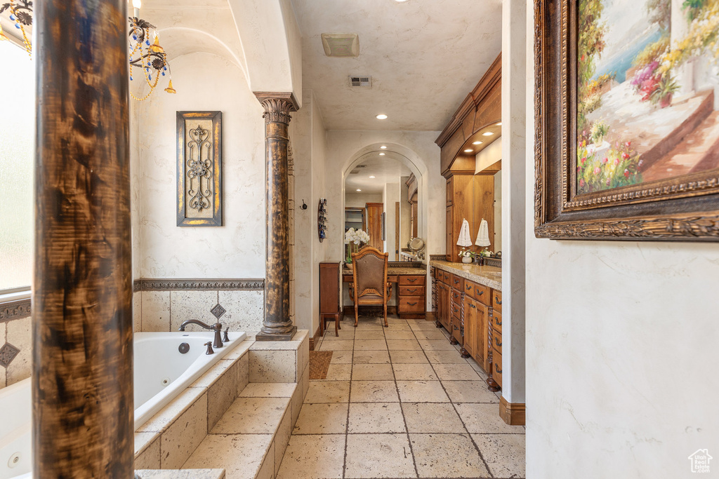 Bathroom featuring vanity, ornate columns, a jetted tub, and stone tile flooring