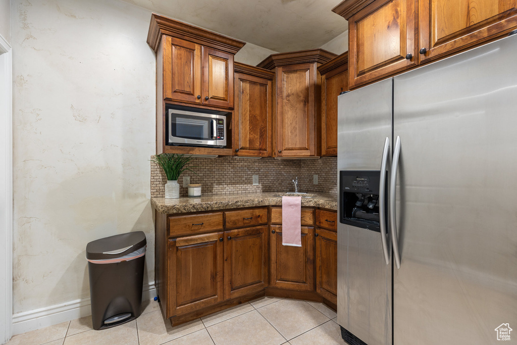 Kitchen with stainless steel appliances, decorative backsplash, stone countertops, brown cabinets, and light tile patterned floors