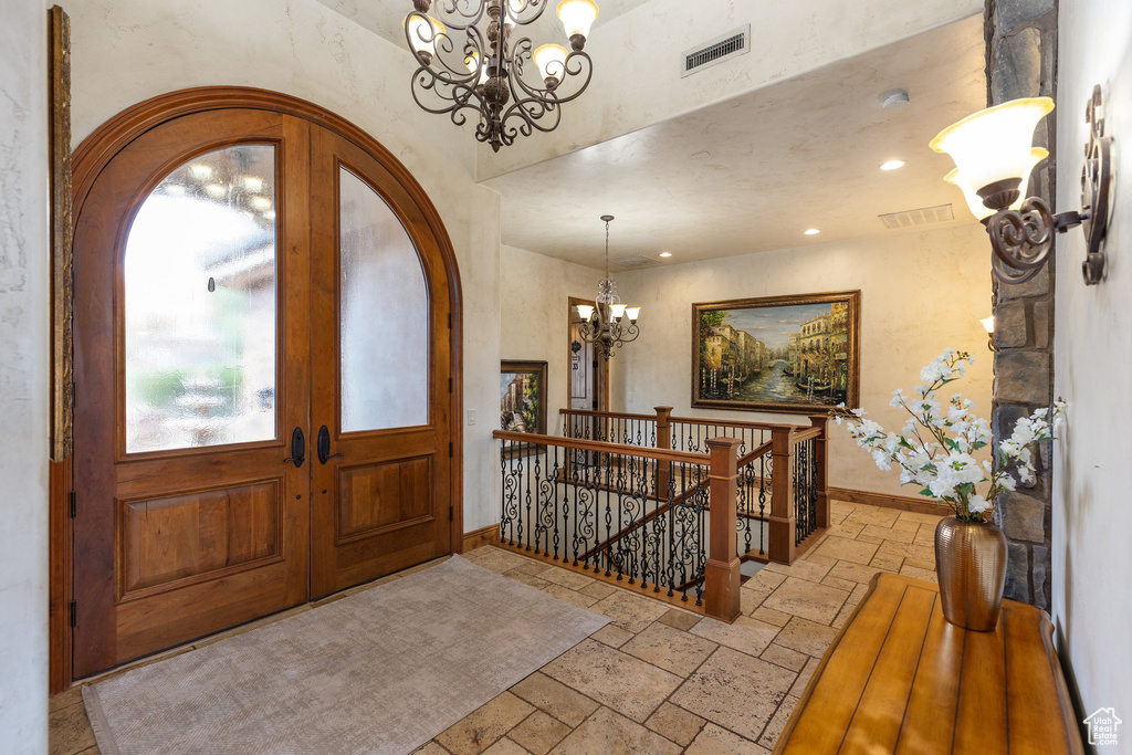 Foyer with stone tile flooring, a chandelier, french doors, arched walkways, and recessed lighting