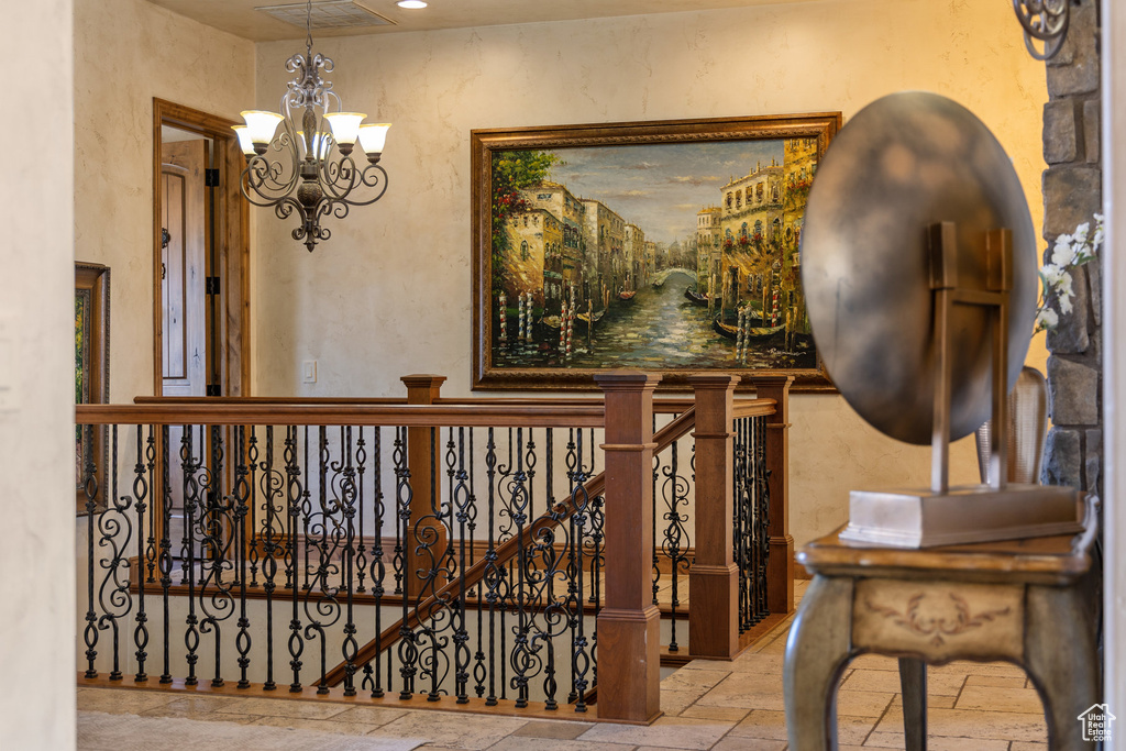 Stairway featuring stone tile floors, a chandelier, and a textured wall