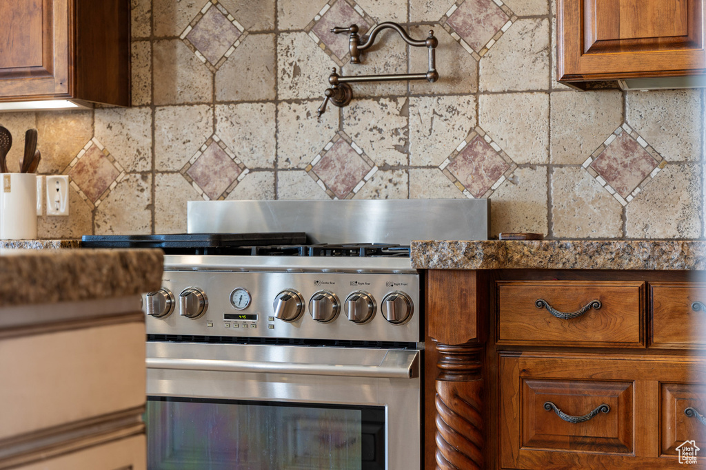 Detailed view of high end range, pot filler, tasteful backsplash, and brown cabinets