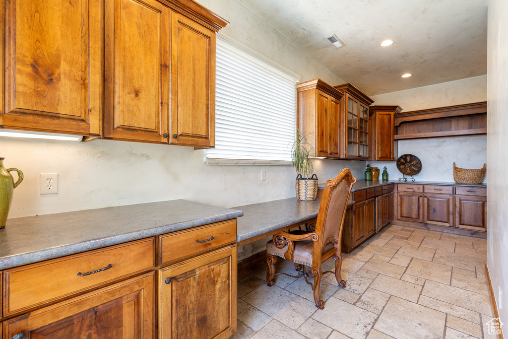 Kitchen with built in desk, brown cabinetry, stone tile flooring, and recessed lighting