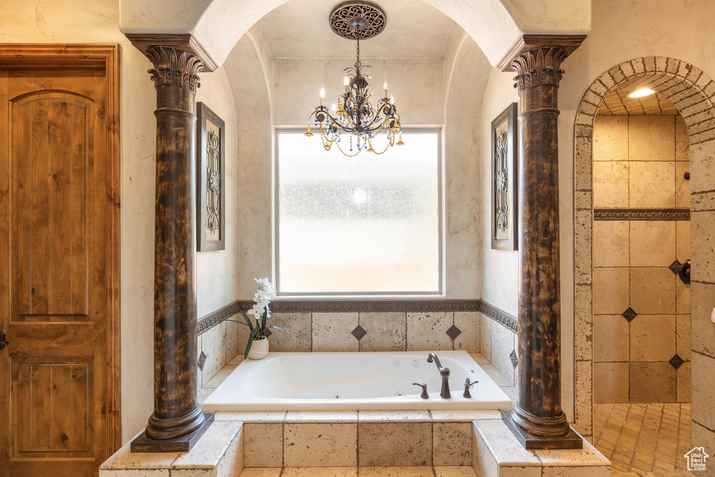 Full bathroom featuring a jetted tub, a chandelier, and decorative columns