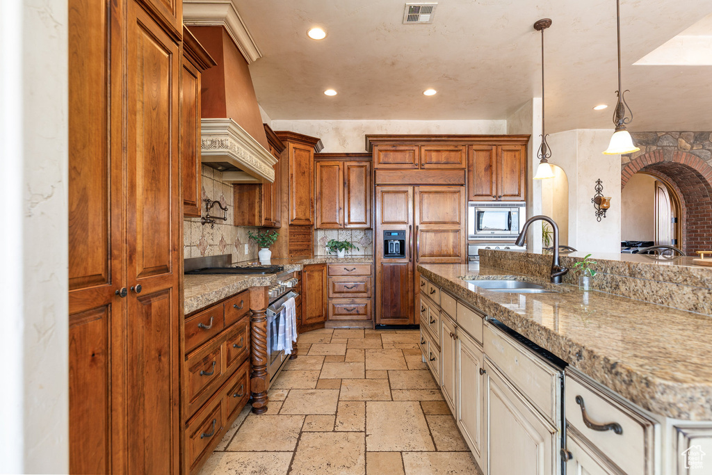 Kitchen with built in appliances, stone tile flooring, arched walkways, recessed lighting, and premium range hood