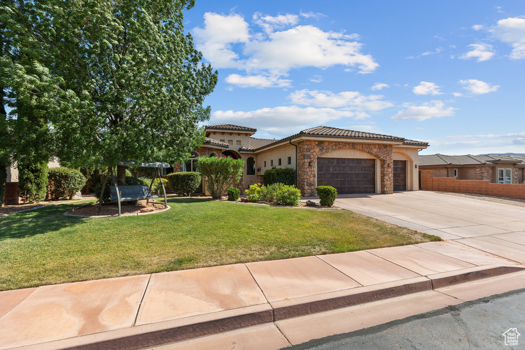 Mediterranean / spanish-style house with an attached garage, driveway, stone siding, a front lawn, and a tile roof