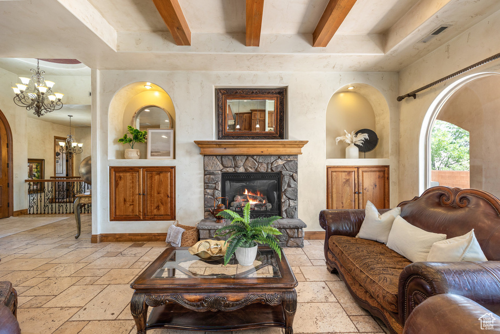 Living room with stone tile floors, a chandelier, a stone fireplace, beam ceiling, and arched walkways